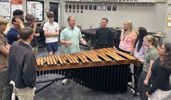 percussion teacher showing how to play the marimba to a group of students 