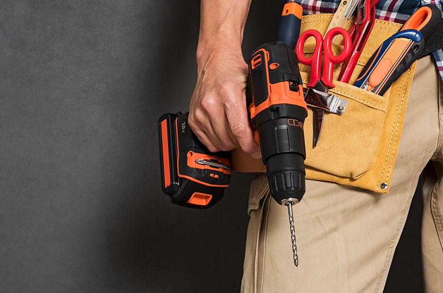 Closeup of a handy man's belt with the wearer holding a drill in his right hand.