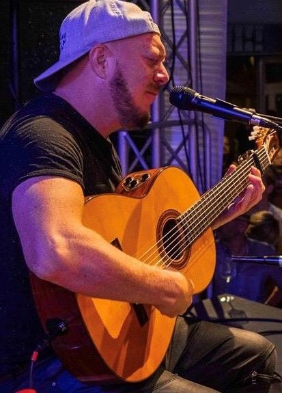 Man wearing a baseball cap backwards playing a guitar on stage and singing.