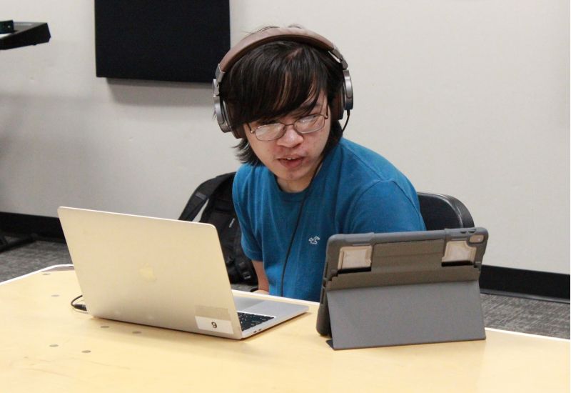 student wearing headphones and sitting at desk with a laptop and tablet