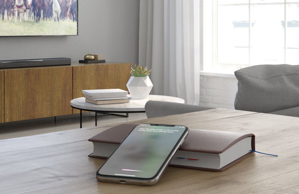 Modern living room with flat screen on wall in background and a smartphone with an app on table in foreground.