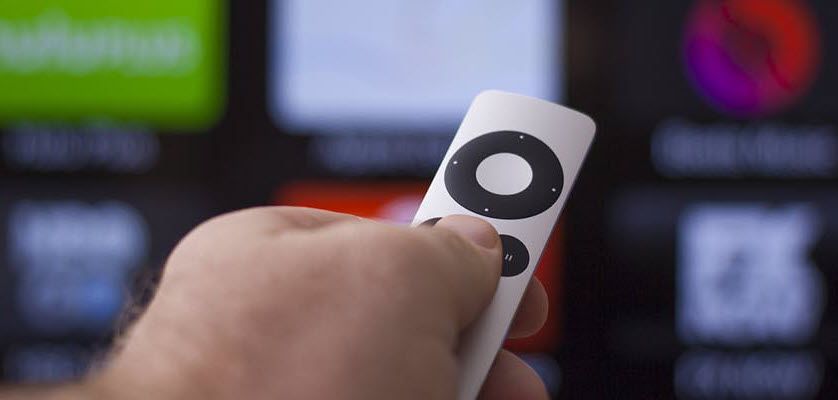 Closeup of hand with tv remote pointing at a tv screen showing streaming channel options.