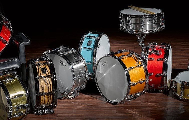 A collection of snare drums arranged haphazardly on a darkened stage.