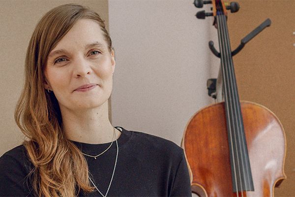 Woman posing for picture in studio with cello in background.