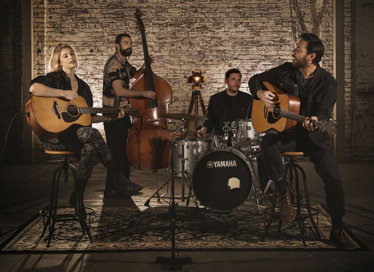 Man and woman playing acoustic guitars with a drummer and upright bass player accompanying.