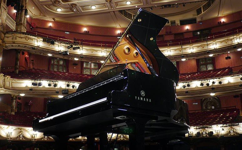 Concert grand piano center stage in an empty and opulent concert hall.