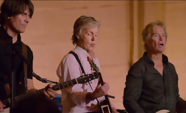 Paul McCartney on stage with two other performers playing guitars.