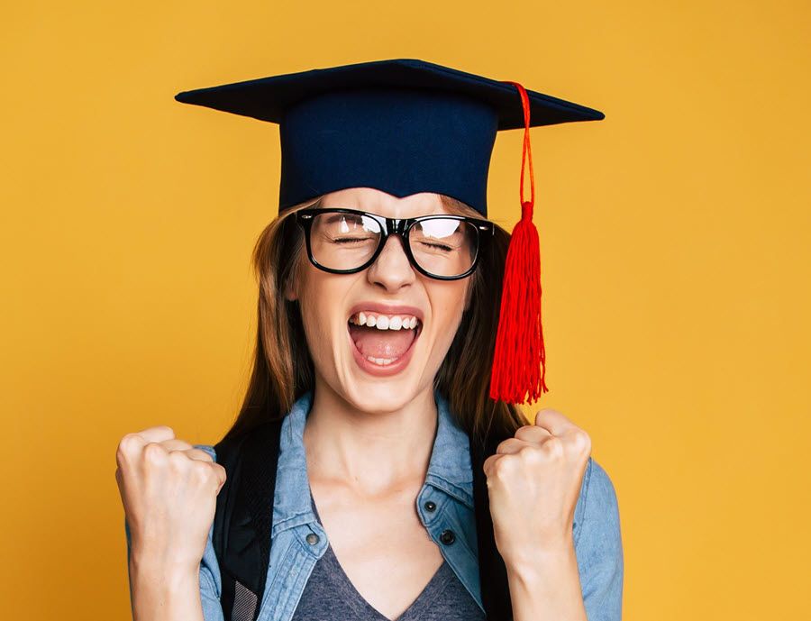 Young woman in mortar board with tassel expressing joy.