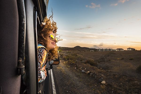 Young caucasian woman travel outside the car with wind in the curly hair, motion and movement on the road discovering new places during a nice sunset.