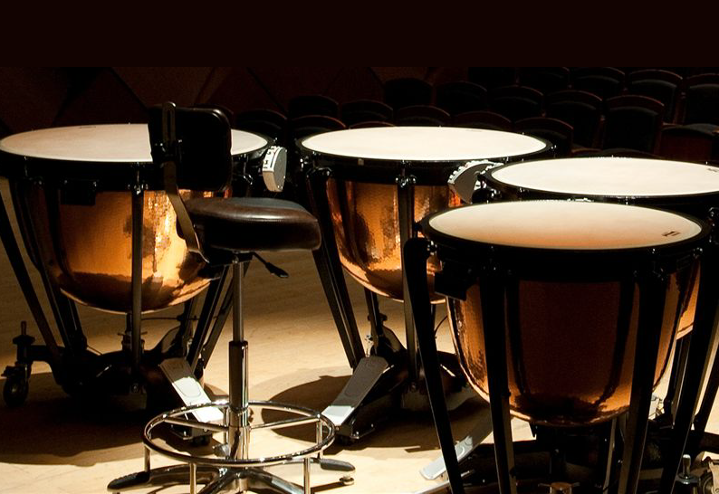 Set of timpani under a spotlight on a darkened stage.