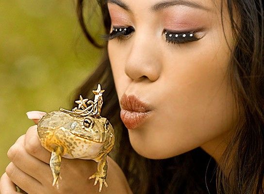 Beautiful woman puckered up to kiss holding a frog that is wearing a small crown.