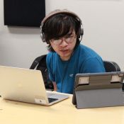 student wearing headphones and sitting at desk with a laptop and tablet