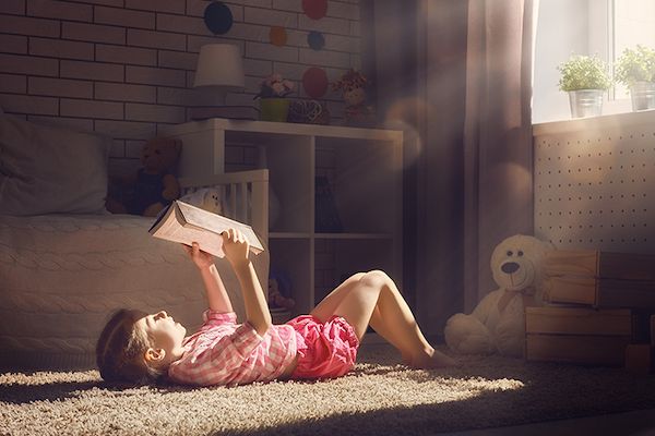 Young girl reading a book on the floor of her room.