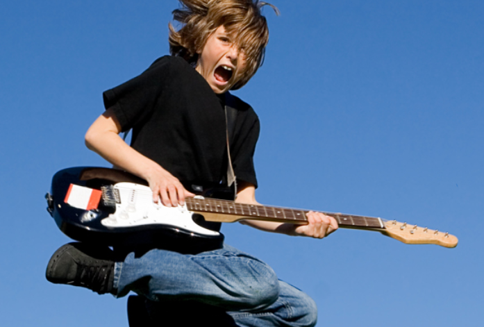 Young boy jumping in air while playing electric guitar.