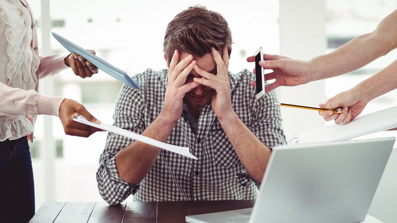 overwhelmed teacher with head in his hands while people are shoving a piece of paper, a cell phone, a pencil, a clipboard and an envelope toward him
