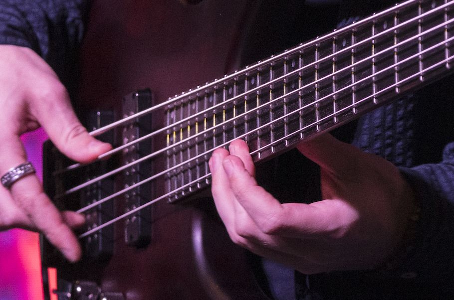 Closeup of hands playing electric bass guitar.