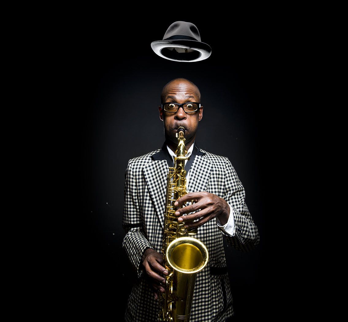 Man playing the sax with fedora popping off in surprise or effort.