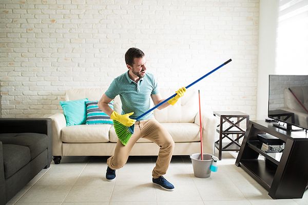 Man having fun playing air guitar with a broom in the living room.