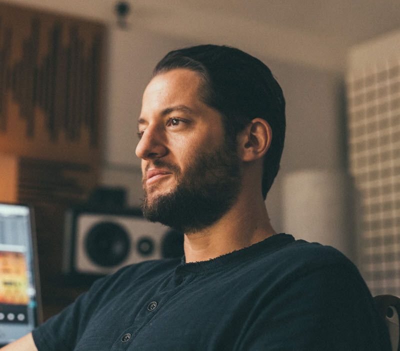 Young man with short dark hair and short beard seen in profile in a sound studio.