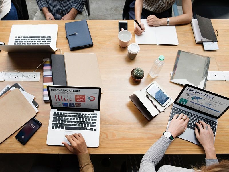 people sitting around conference room table on laptops