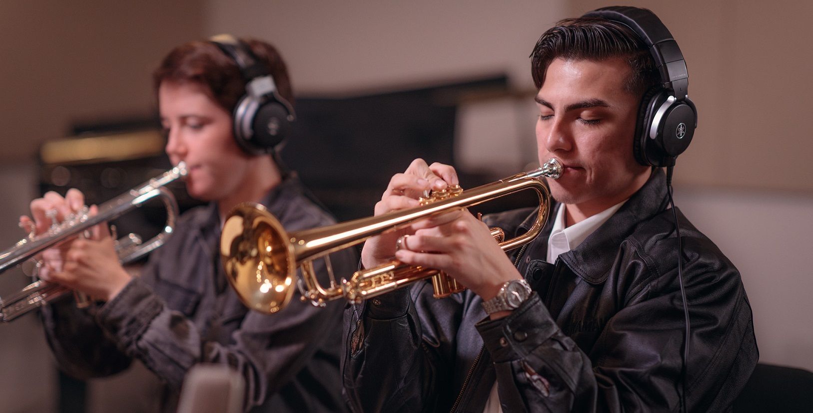 two students playing trumpets and wearing headphones