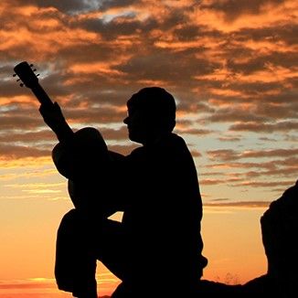 Silhouette of a man playing guitar in front of a beautiful sunset.