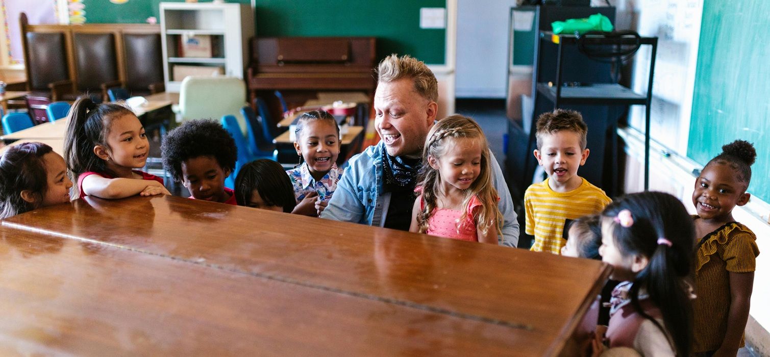 elementary music teacher at piano with students all around him