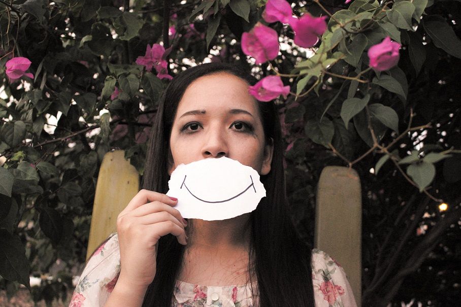 sad woman holding up smiling drawing in front of mouth