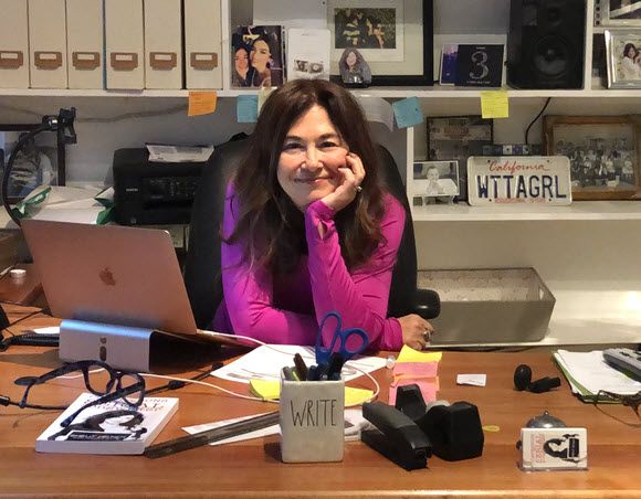 Woman with log dark hair at a desk in a home office smiling for camera.