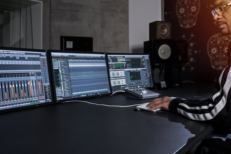 Man at computer keyboard with three screens in front of him displaying sound data output.