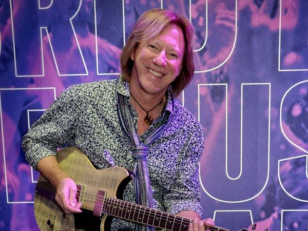 Robbie Calvo in patterned casual shirt and scarf smiling at camera while playing his electric guitar.