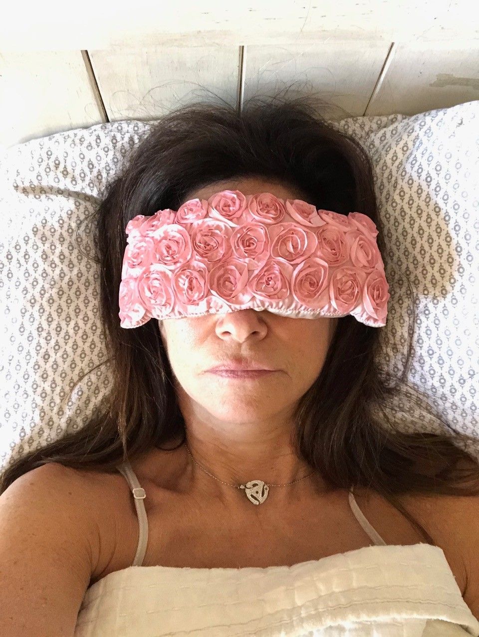 Shelly Peiken laying face up in bed wearing a floral eye mask.