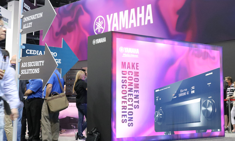 Convention hall with people lined up and large video screens with Yamaha and other headlines.