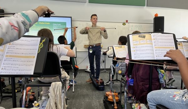Music educator Tanner Otto showing students how to hold a bow