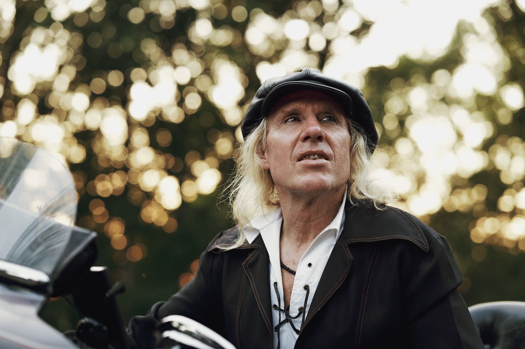 Man outside looking up with blonde long hair and black leather hat.