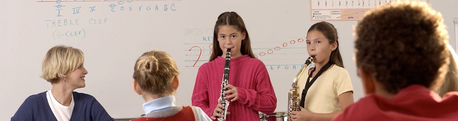 Two young female students playing clarinet and saxophone for teachers.
