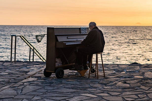 Elderly man playing a piano in front of the ocean.