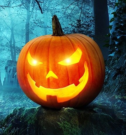 A lit up jack-o-lantern with a spooky, foggy forest scene in background.