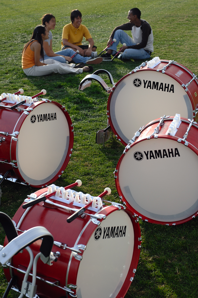 Students sitting on a field with marching bass drums.