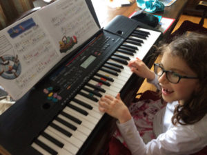 A child smiling as she plays a portable digital keyboard.
