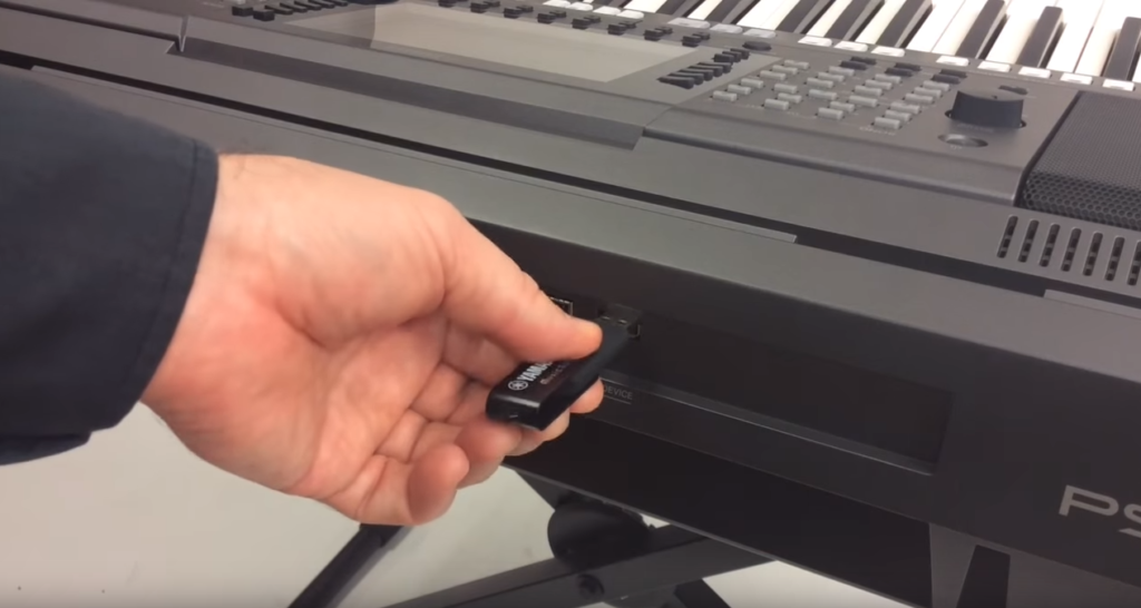A hand inserting a USB flash drive into the front of a digital keyboard.