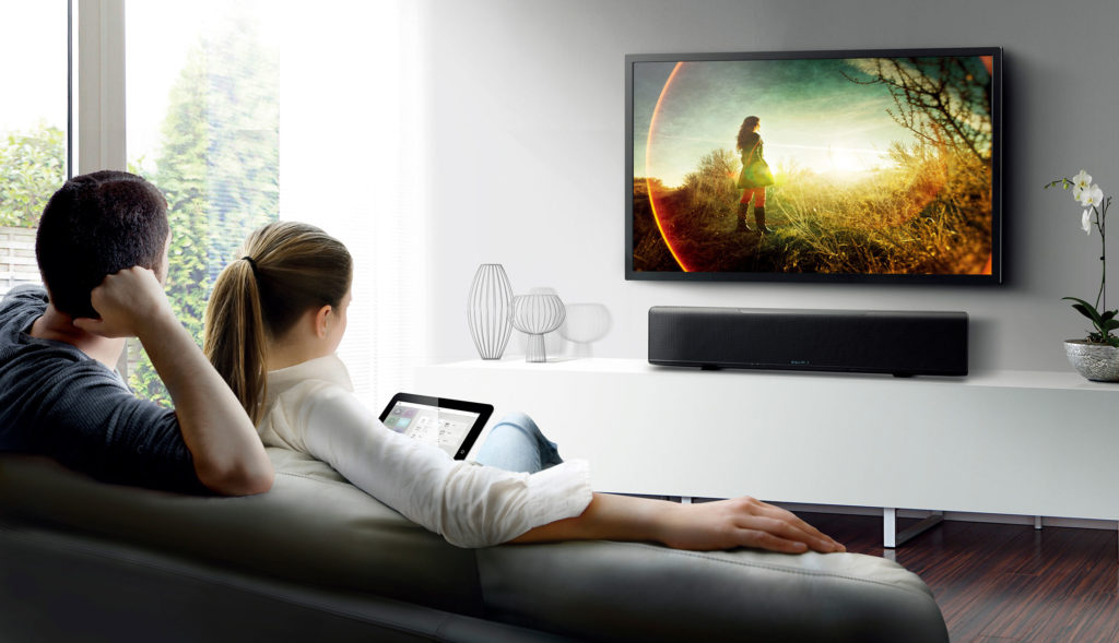 Man and woman sitting in living room in front of television with sound bar.