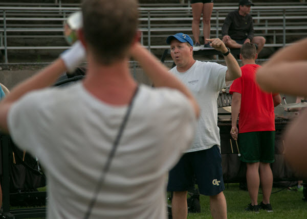 Band leader conducts practice on a football field with young brass player in foreground.