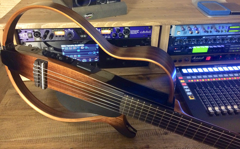 Electric guitar with open body on side on table next to sound boards and sound equipment.