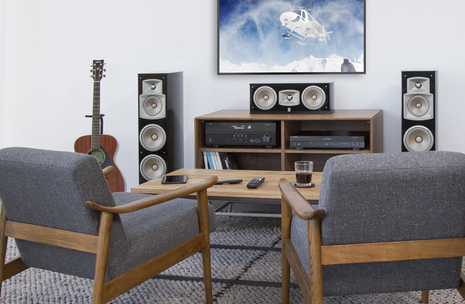Living room setting with two chairs facing a large flat screen with home theater equipment, including receiver and surround sound speakers.