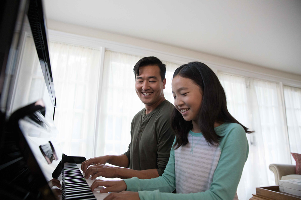 Young girl and her father play piano together.