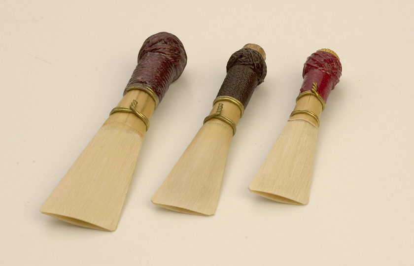 Three bassoon reeds, lined up largest to smallest, left to right.