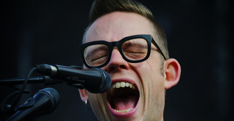 Man singing into a microphone with his mouth open wide.