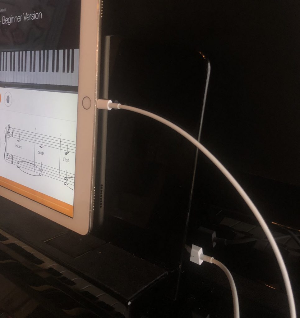 View of a tablet from the right hand side showing the cable connection on tablet and the other end of the cable plugged into the piano.
