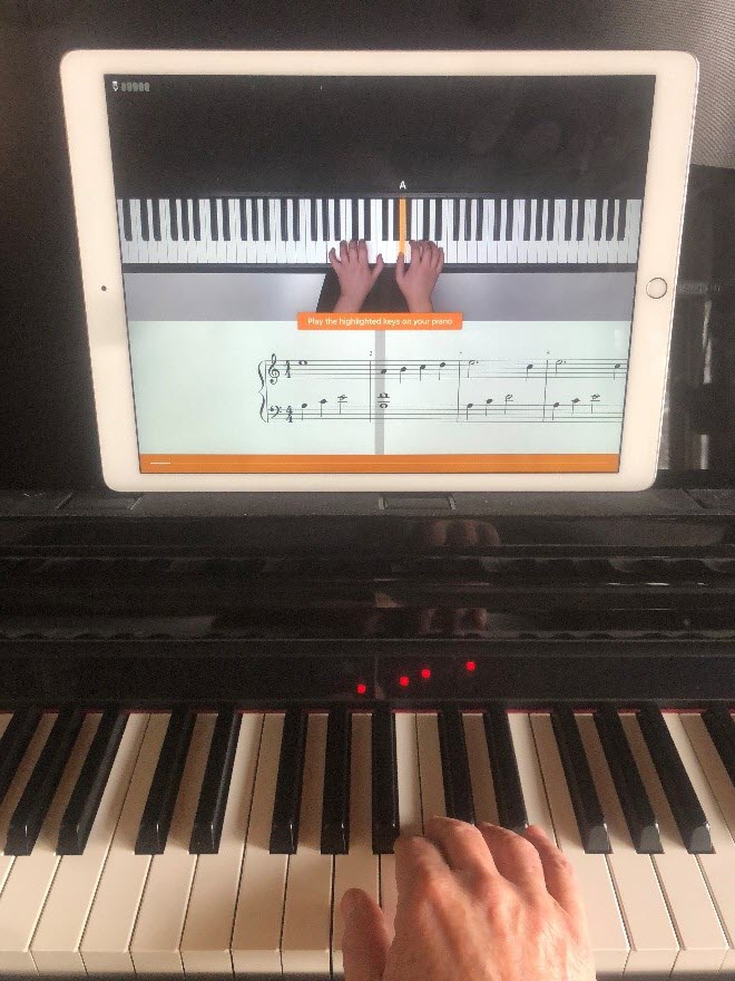 Hands on a piano keyboard playing the music annotation and hand placement visible on a tablet screen on the music tray above the hands.